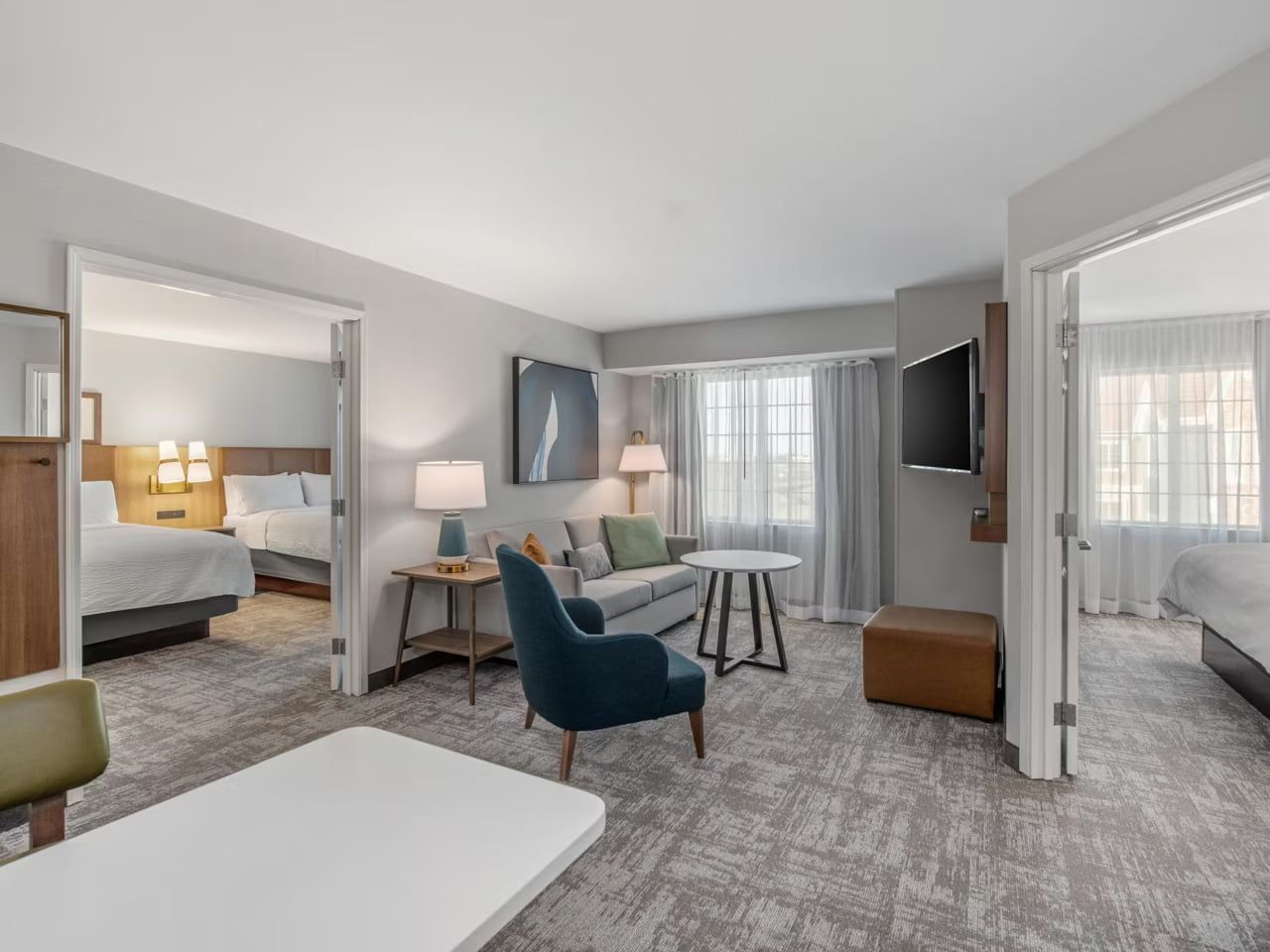 Una habitación de hotel con cama, sofá, sillón, una mesita, televisión y ventana con cortinas.