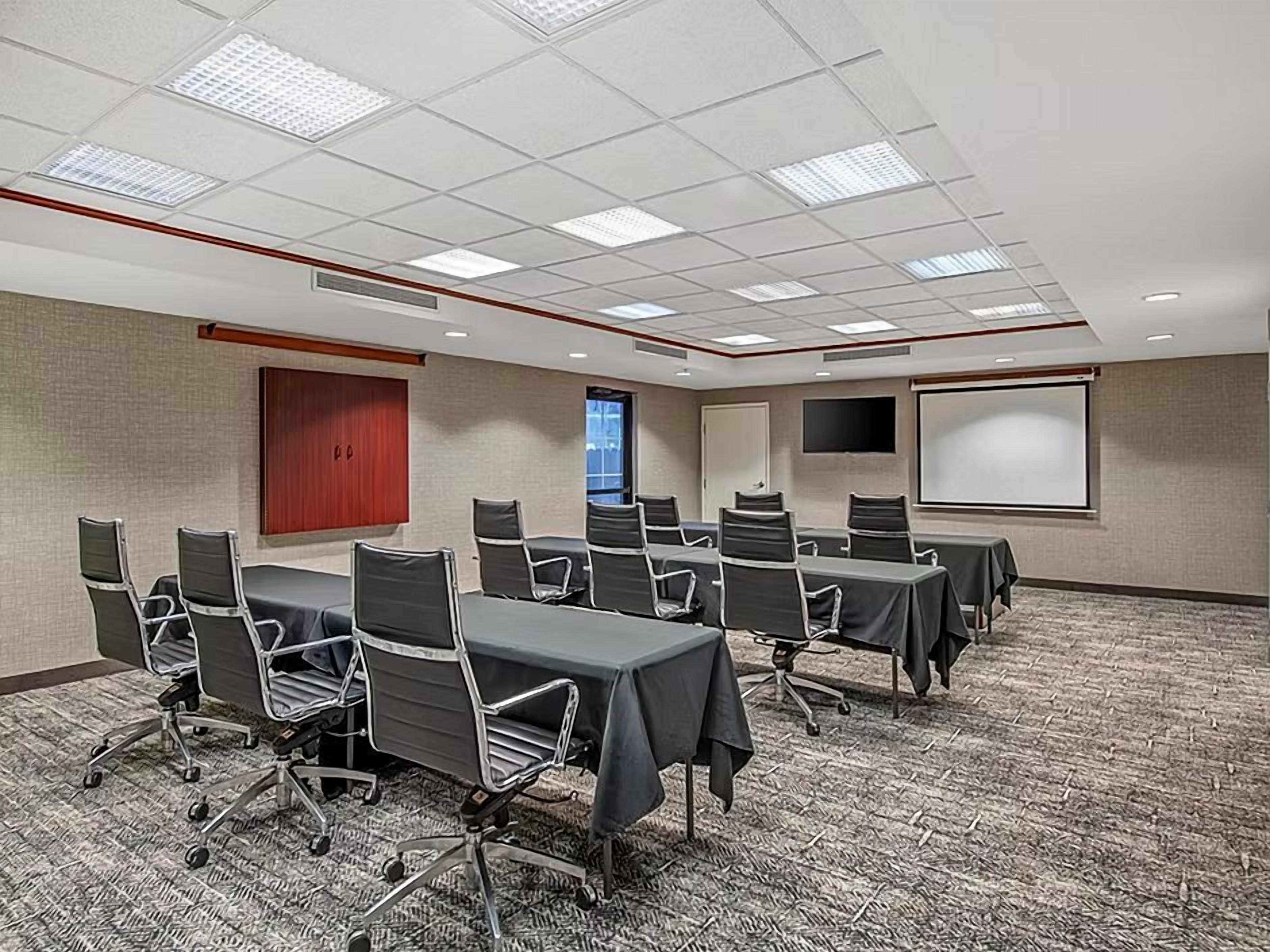 A conference room with a carpeted floor, multiple tables with chairs, a projector screen, and a door.