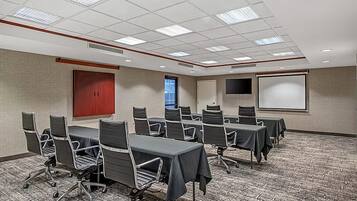 A conference room with a carpeted floor, multiple tables with chairs, a projector screen, and a door.