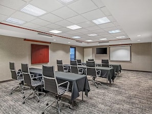 A conference room with a carpeted floor, multiple tables with chairs, a projector screen, and a door. - Spacious Suite w/ Kitchen | Free Breakfast (Rocklin)