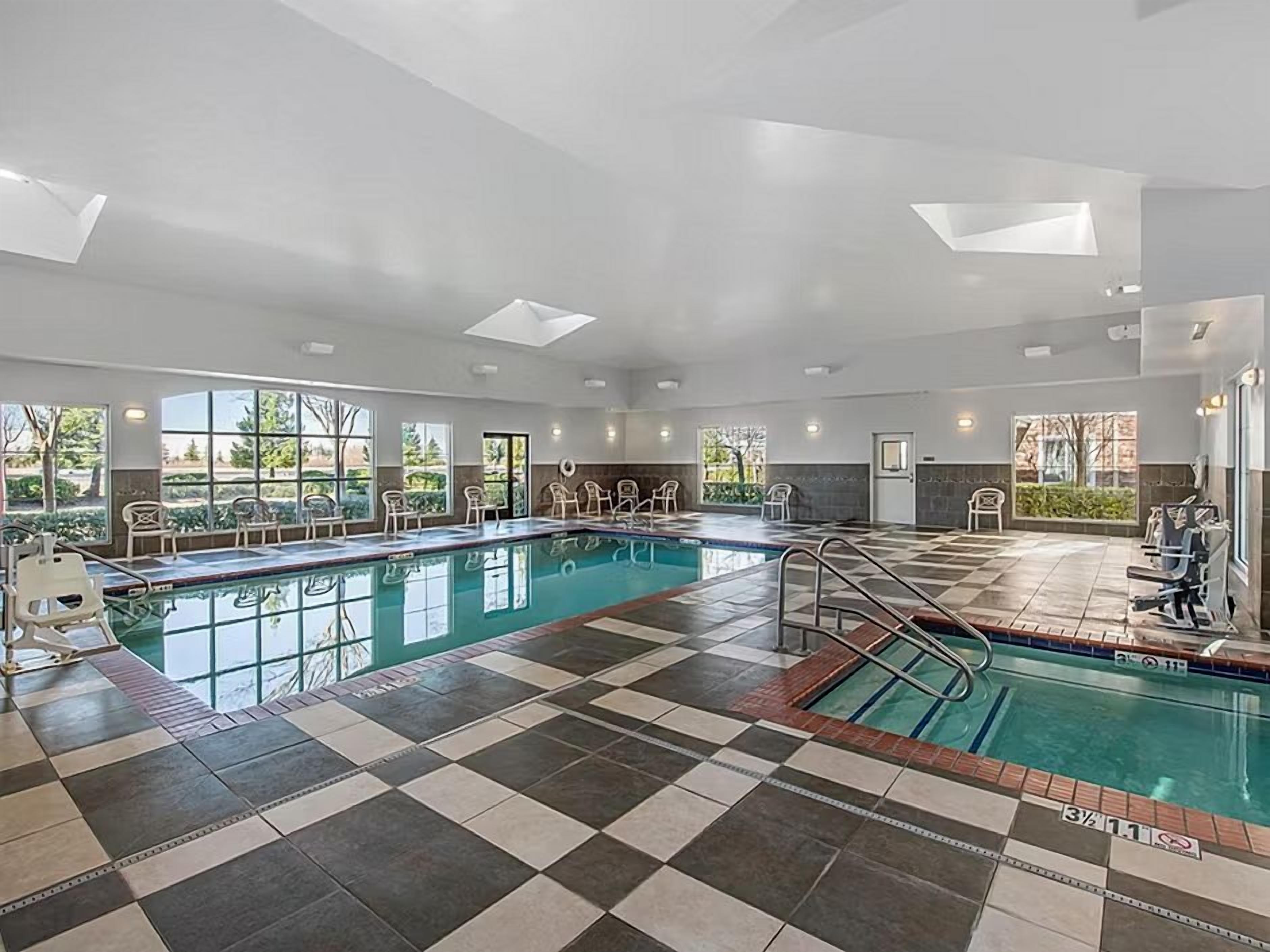 A large indoor swimming pool with checkered flooring, multiple windows, and a sunlit ceiling.