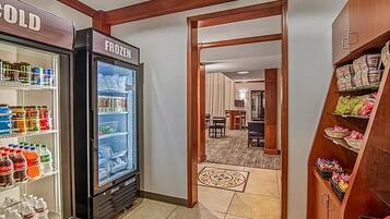 A hotel lobby with a refrigerated display case labeled 'COLD' and 'FROZEN,' a carpeted area leading to a dining room, and a snack shelf.