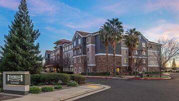 A multi-story hotel with a stone facade, a sign indicating it's a Staybridge Suites, and a parking lot in front.