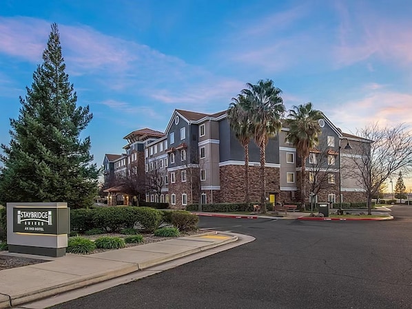 A multi-story hotel with a stone facade, a sign indicating it's a Staybridge Suites, and a parking lot in front. - Accessible Suite w/ Kitchen, Pool & Free Breakfast (Rocklin)