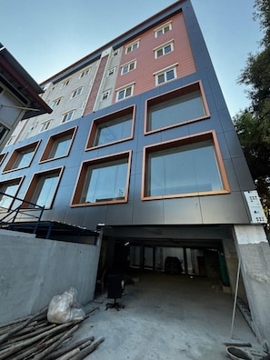 A multi-story building with a modern architectural design, featuring large windows and a mix of red and grey facade colors. - Deluxe King Room The Whitefield (Bengaluru)