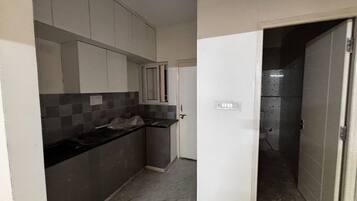 A narrow kitchen with grey cabinets, a black countertop, and a tiled backsplash.