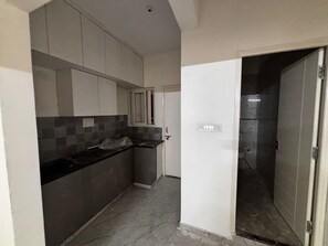 A narrow kitchen with grey cabinets, a black countertop, and a tiled backsplash. - Deluxe King Room The Whitefield (Bengaluru)