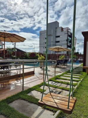 A wooden swing set with ropes, a pool, and umbrellas in a patio area.