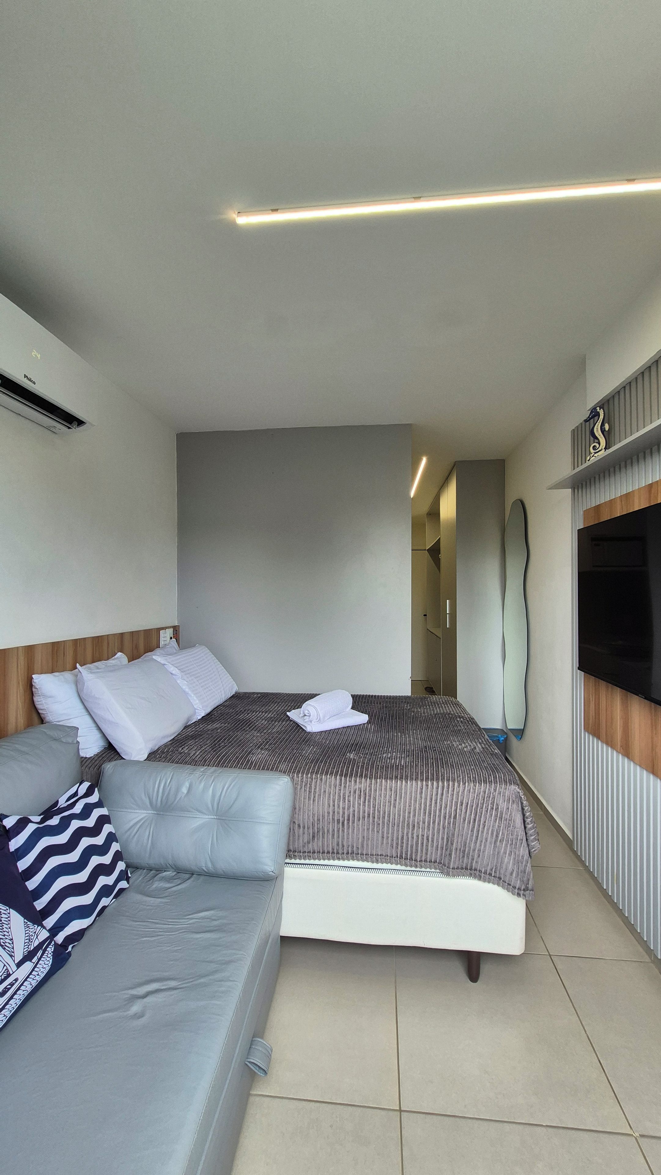 Quarto de hotel com cama, sofá, televisão e espelho.