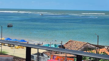 Une vue sur la plage depuis un balcon, avec un ciel dégagé, une plage de sable et quelques parasols.
