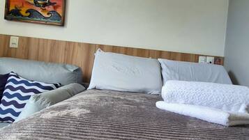 Une chambre d’hôtel comprenant un lit, des oreillers, une tête de lit, un climatiseur fixé au mur et une œuvre d’art encadrée.