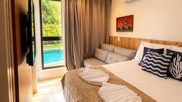 Quarto de hotel com cama, televisão, ar condicionado, quadro e vista para uma piscina.