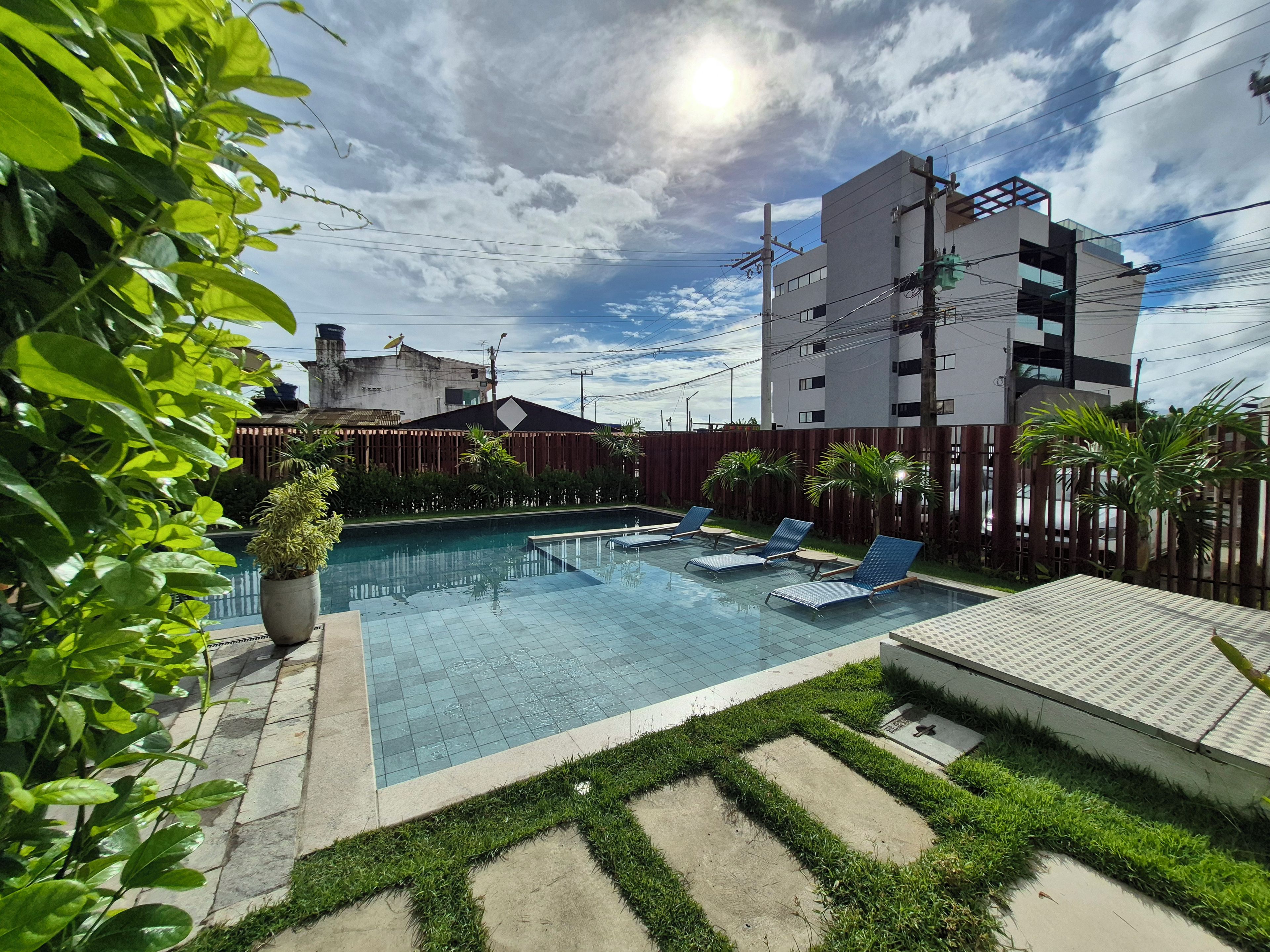 A swimming pool with lounge chairs, surrounded by a wooden fence and greenery.