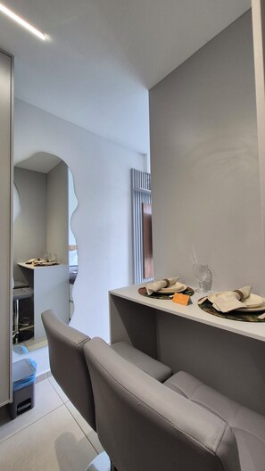 Une chambre d’hôtel moderne avec un coin repas comprenant une table mise avec des assiettes, des verres et une serviette. Un miroir est accroché au mur et une chaise se trouve au premier plan.