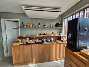 Une petite cuisine équipée d’un climatiseur intégré, d’un réfrigérateur, ainsi que d’une variété d’aliments et d’ustensiles de cuisine disposés sur le plan de travail.