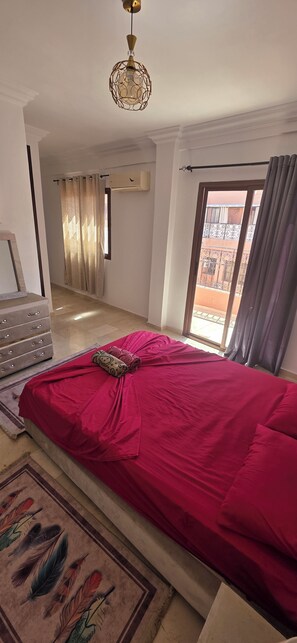 Une chambre à coucher comprenant un lit, une commode, une fenêtre avec des rideaux et un luminaire au plafond.
