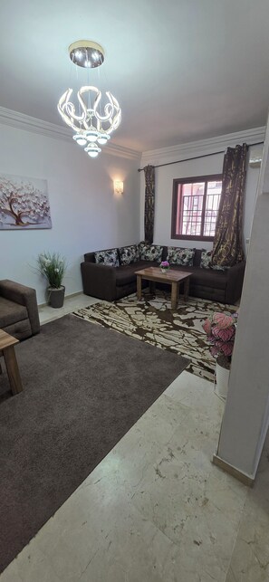 A living room with a sofa set, a coffee table, a chandelier, a painting, and a window with curtains. - Appartement le palmeraie de guéliz Marrakech (Marrakech)