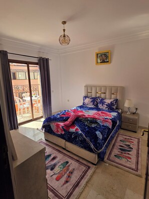 A bedroom with a bed, a nightstand, a lamp, a ceiling light, a sliding door to a balcony, and a framed picture on the wall. - Appartement le palmeraie de guéliz Marrakech (Marrakech)