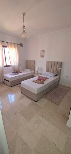A hotel room with two beds, a ceiling fan, a window with curtains, and a small rug. - Appartement le palmeraie de guéliz Marrakech (Marrakech)