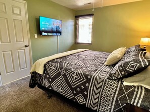 A bedroom with a bed, a television mounted on the wall, a window with blinds, and a door. - Tranquil 1-BR condo/St. George/Pools/Gym/near Zion NP & Tuacahn (St. George)