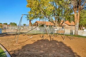 A playground with swings and a slide, surrounded by a fence and trees. - Tranquil 1-BR condo/St. George/Pools/Gym/near Zion NP & Tuacahn (St. George)