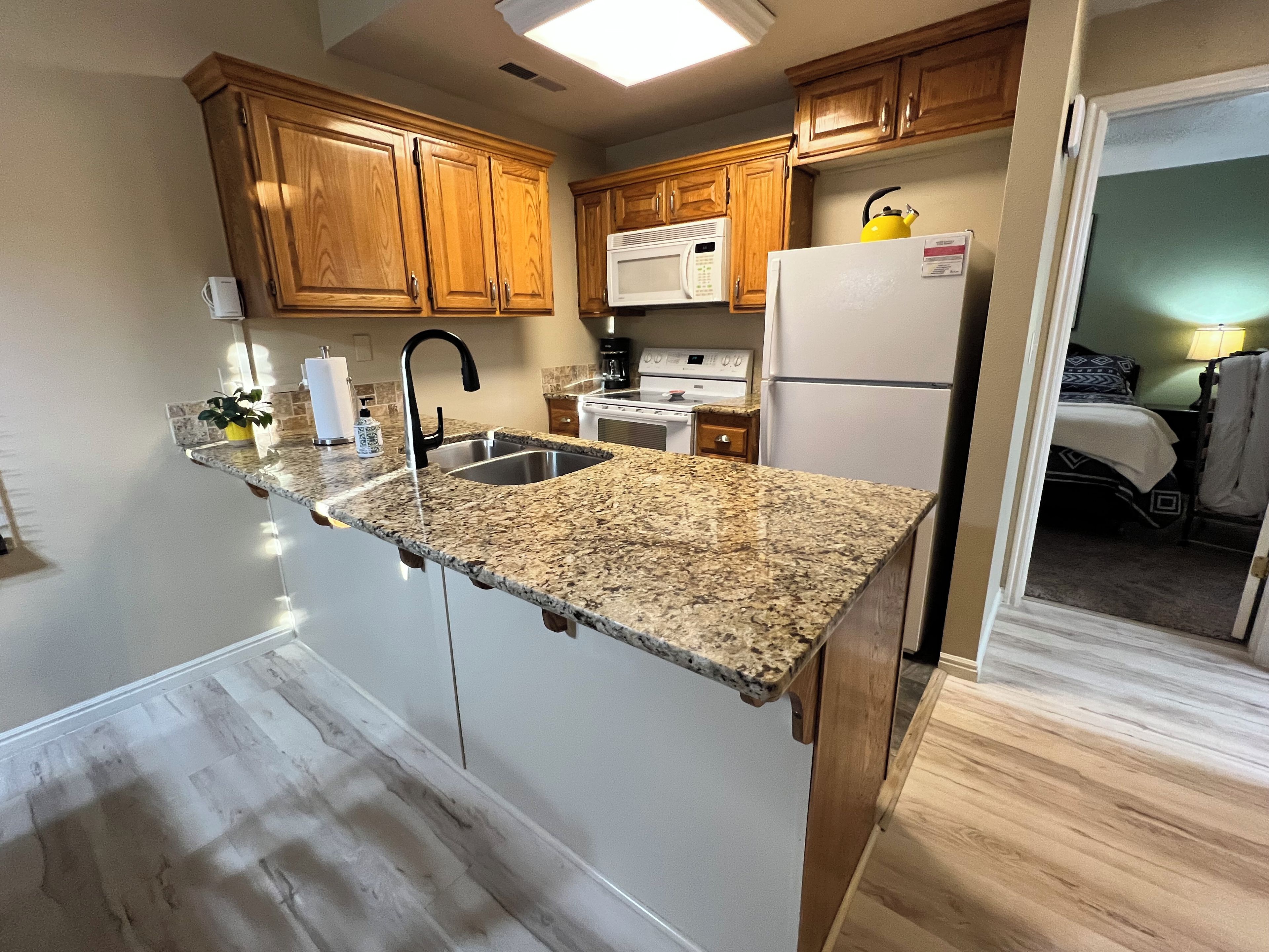 A kitchen with granite countertops, wooden cabinets, a stainless steel sink, a microwave, a stove, and a refrigerator.