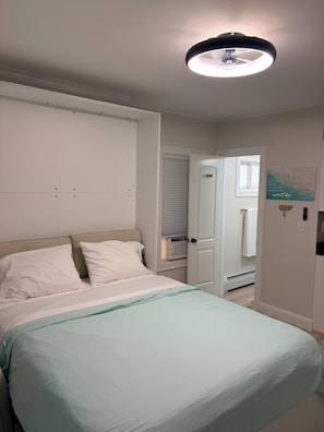 A bedroom with a bed, a bedside table, a ceiling light, a door, and a wall with a picture. - Steps to Beach & Pier Stylish OOB Studio + Parking (Old Orchard Beach)