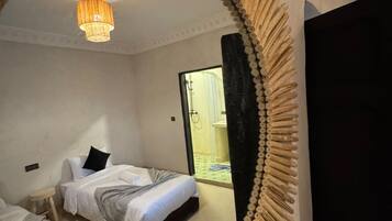 Un dormitorio con dos camas, una araña y vista a un baño a través de un vano.