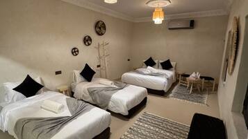 Habitación de hotel con dos camas, una mesita pequeña, una silla, un reloj de pared decorativo y un ventilador de techo.