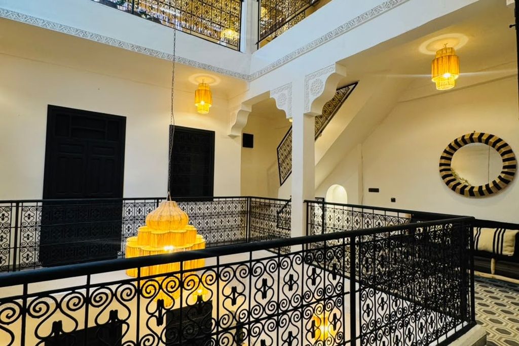 Un interior de varios niveles con barandillas negras decorativas, un candelabro amarillo central y un suelo con diseño.
