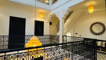 Un intérieur à plusieurs niveaux, agrémenté de rampes noires décorées, d’un grand lustre jaune au centre et d’un sol à motifs.