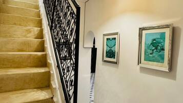 Un escalier avec une rampe noire, un luminaire fixé au mur et deux tableaux encadrés.