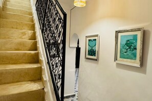 A staircase with a black railing, a wall-mounted light fixture, and two framed pictures. - Riad Timizar (Marrakech)