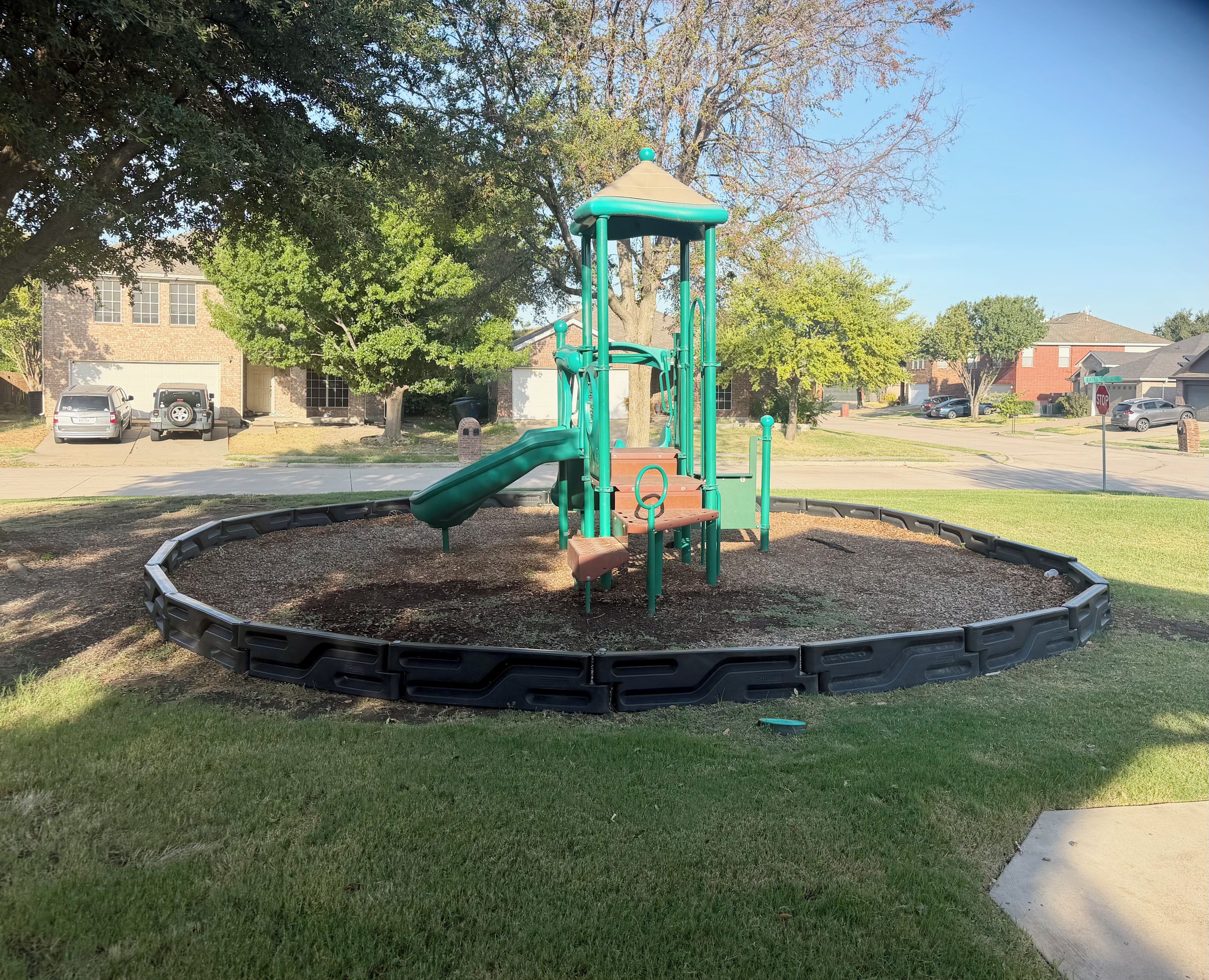 Ein Spielplatz mit Klettergerüst und Rutschen, umgeben von einer begrünten Anlage mit Rasen und Rindenmulch.