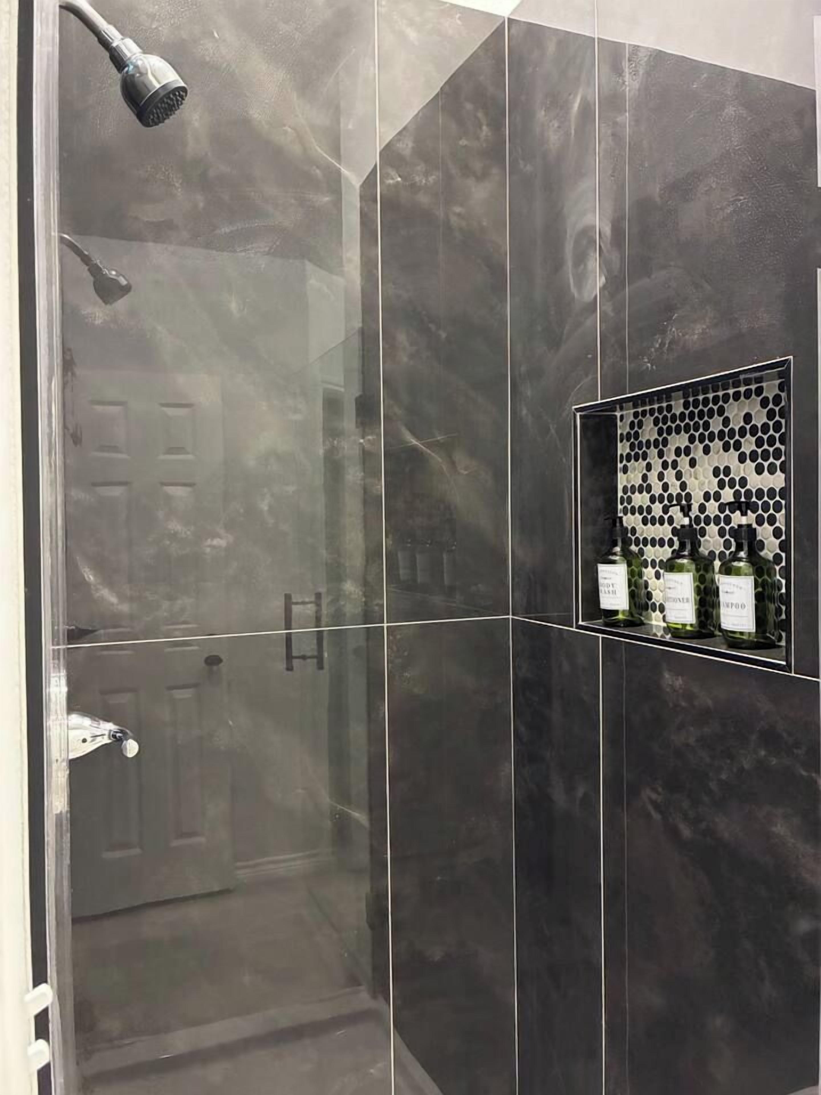 Ein modernes Badezimmer mit einer Duschkabine aus Glas, einem Waschtisch mit Spiegel und einem Ablagebereich für Toilettenartikel.