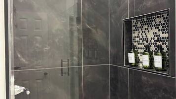 Ein modernes Badezimmer mit einer Duschkabine aus Glas, einem Waschtisch mit Spiegel und einem Ablagebereich für Toilettenartikel.