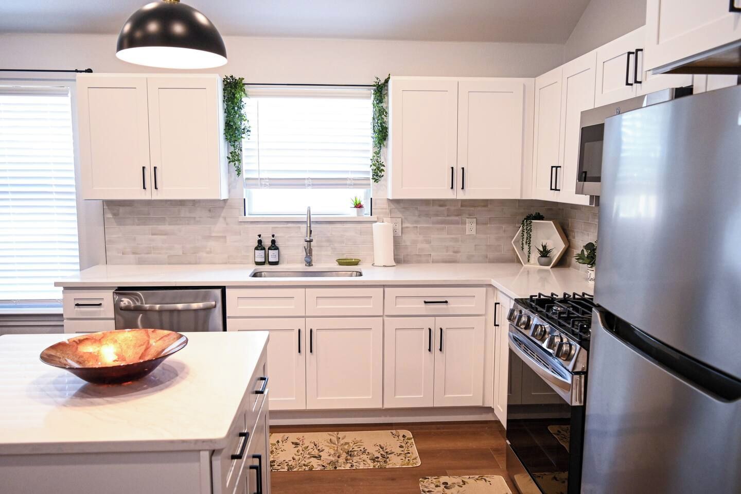 A modern kitchen with white cabinets, a stainless steel refrigerator, a gas stove, and a window with a plant.