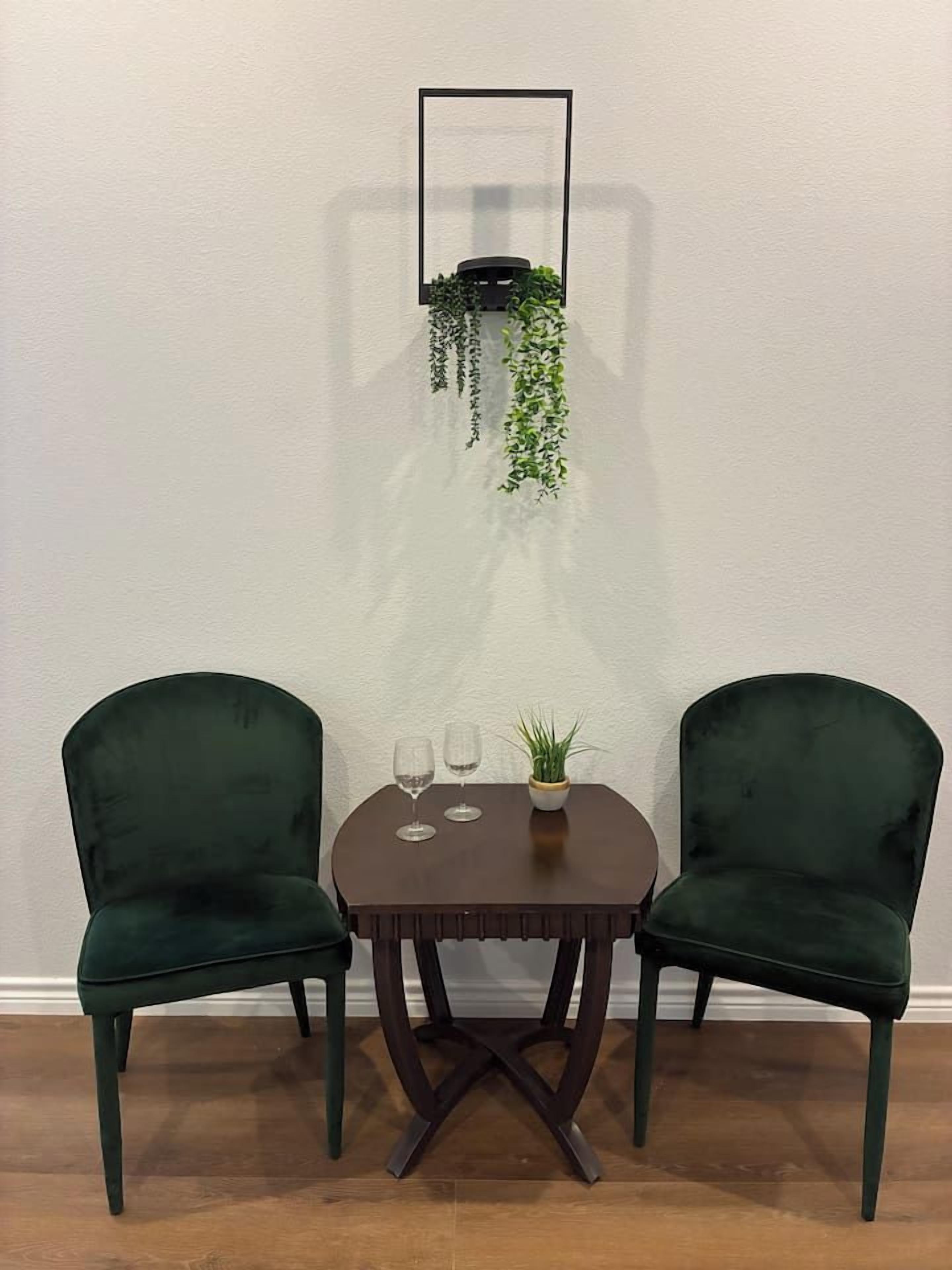 A small dining area with two dark green chairs, a round table, and a hanging plant.