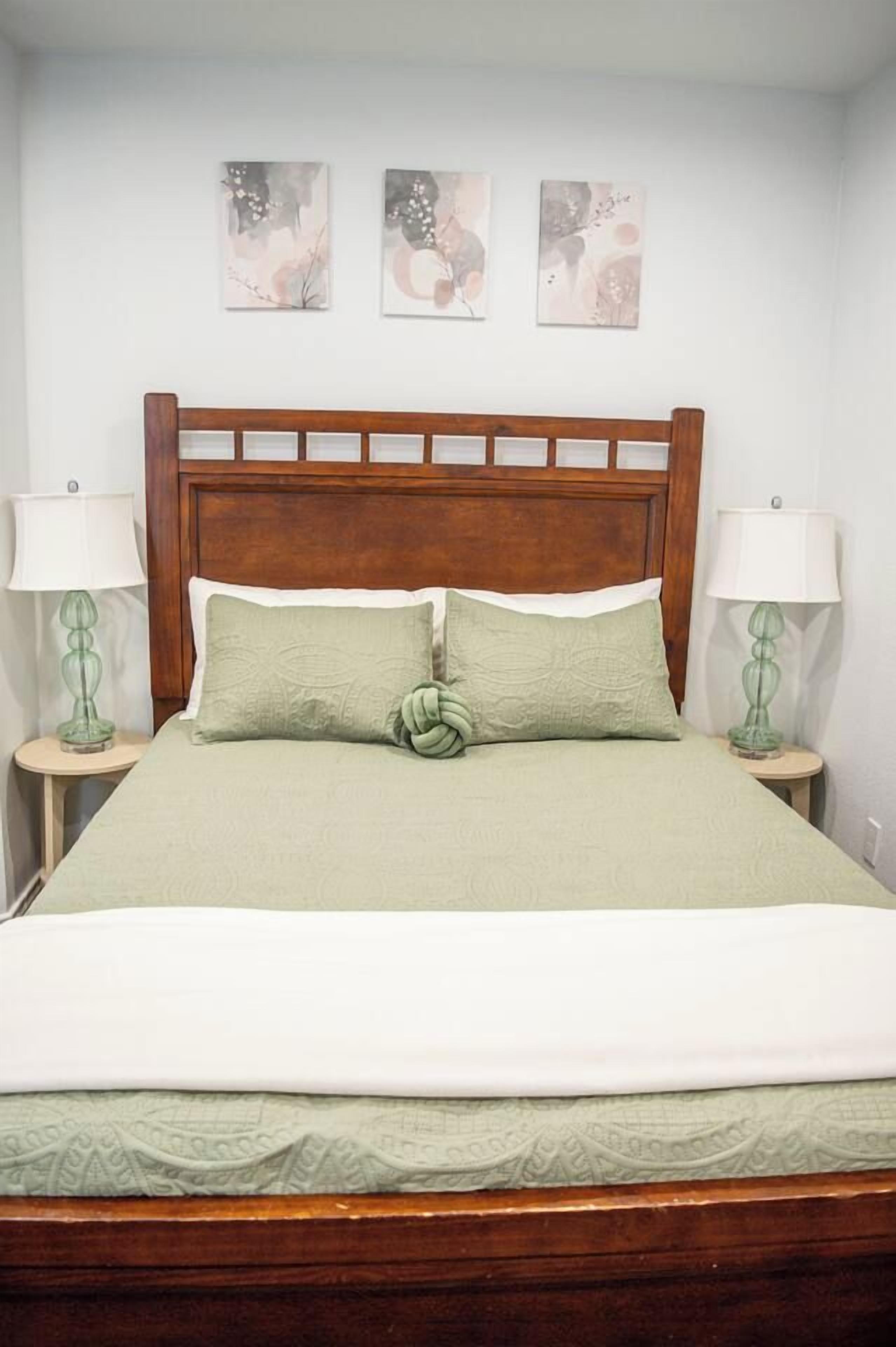 A bed with a wooden headboard, two bedside lamps, and three wall-mounted artworks.