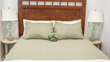 A bed with a wooden headboard, two bedside lamps, and three wall-mounted artworks.