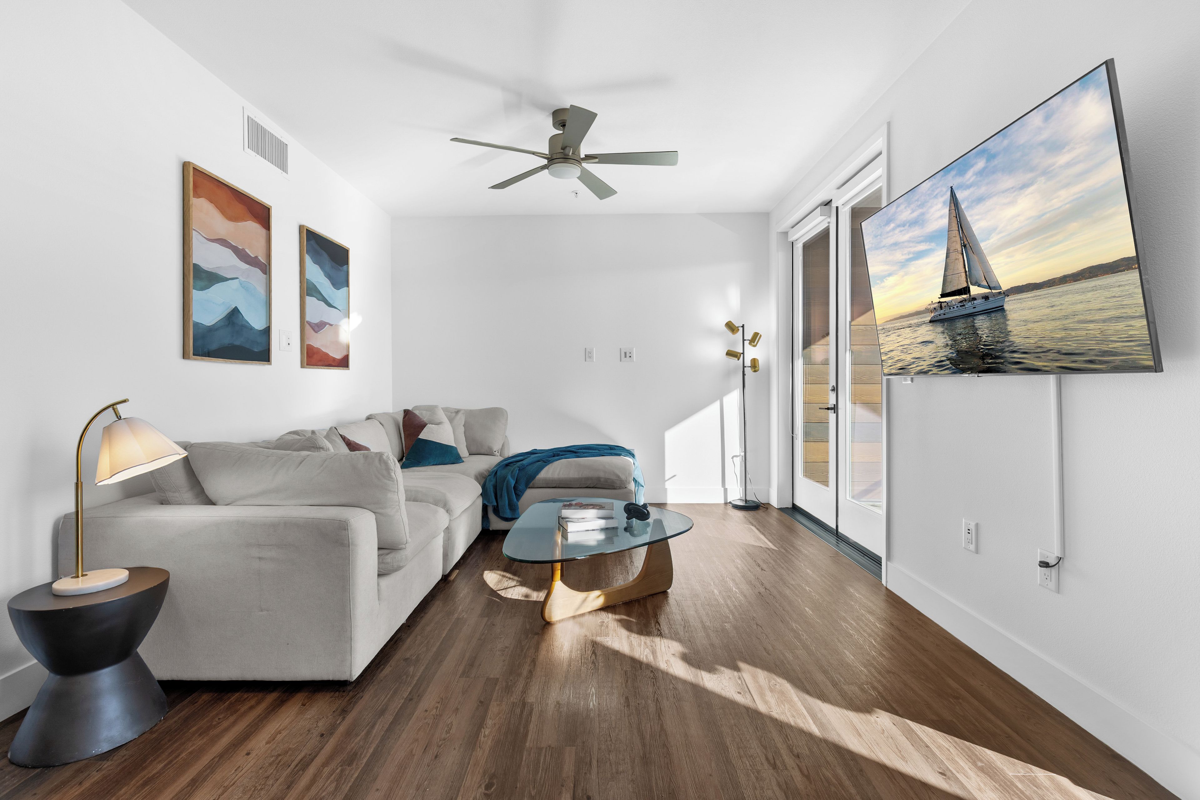 A modern living room with a ceiling fan, a sofa, a coffee table, and a large window with a sailboat view.