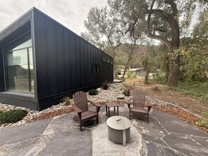 A modern building with a large window, outdoor seating with Adirondack chairs, and a stone patio.