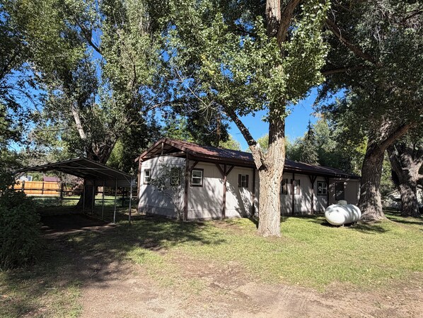 A rustic house with a wooden roof, surrounded by trees and a covered area.