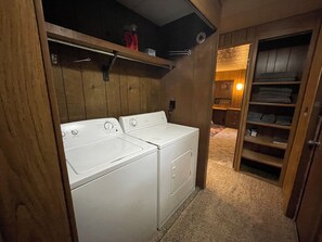 A laundry room with two white front-loading washers and dryers, wooden walls, and a carpeted floor.