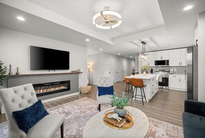 Una sala de estar moderna con chimenea, televisor y una cocina con electrodomésticos de acero inoxidable.