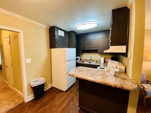 A compact kitchen with dark cabinets, a white refrigerator, a granite countertop, and a trash bin. - First-Floor Highlands Escape: Golf Course Views (Birmingham)