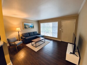 Una sala de estar con sofá, sillón, mesa de centro y un cuadro en la pared.