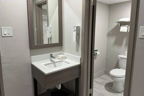 Baño con lavamanos, espejo, dispensador de toallas, inodoro y toallero.