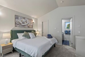 Un dormitorio con cama, mesitas de noche, un cuadro y una puerta que da a un balcón.