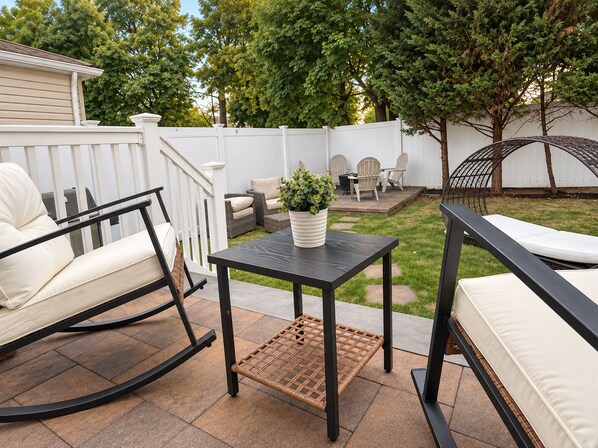 A patio with outdoor furniture, a white fence, and a tree.